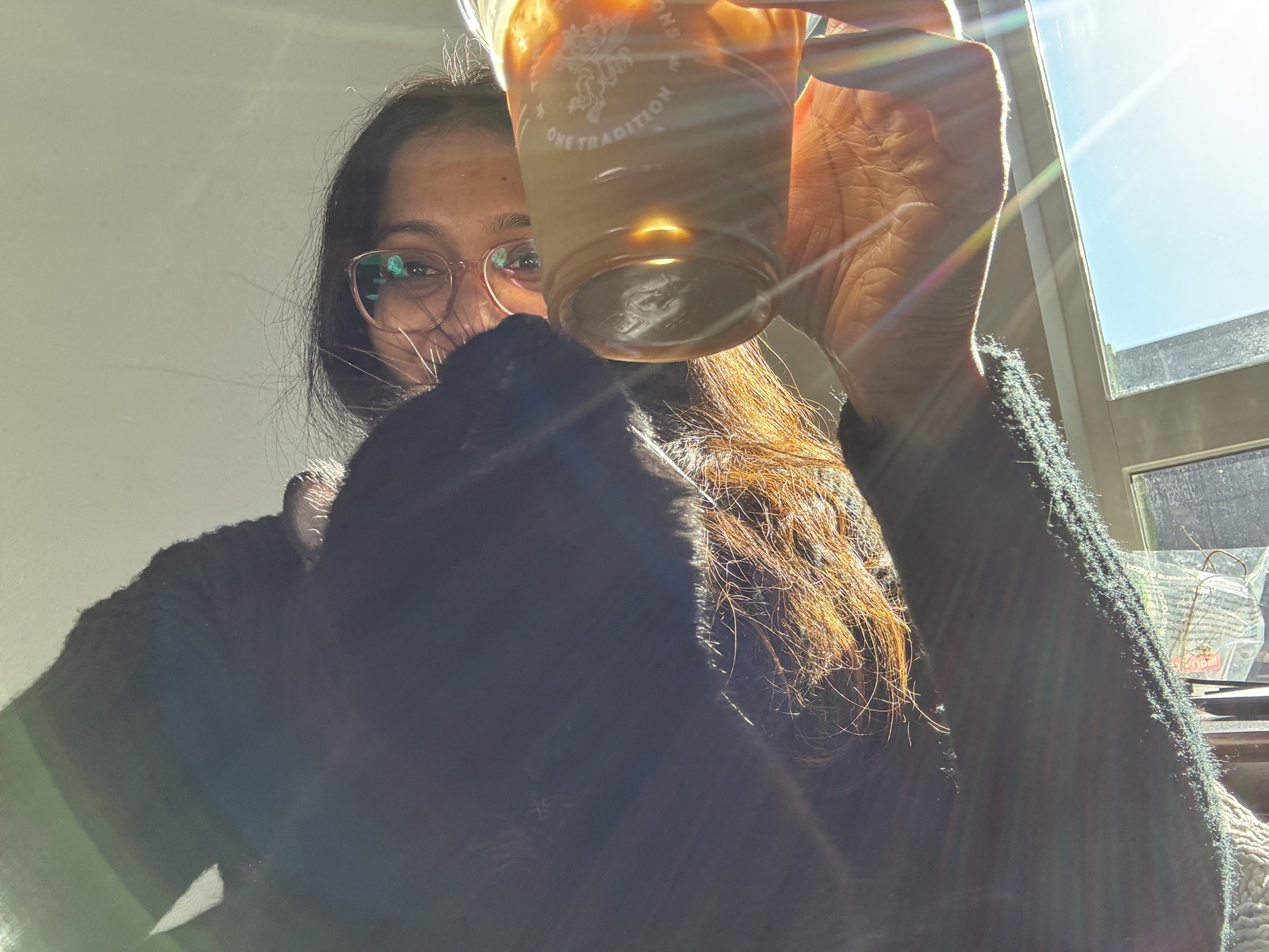 Keerthana with a cat and a drink in the sunlight